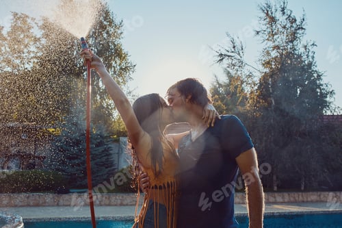 Preview: Couple having fun pour each other with garden hose