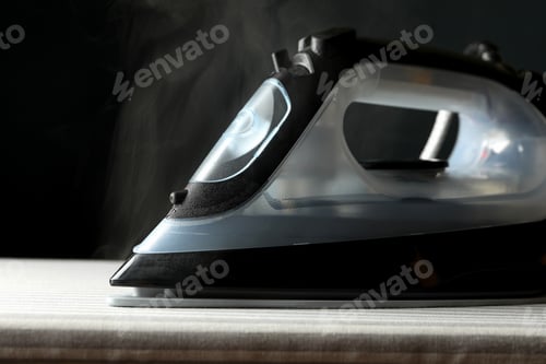 Preview: Iron with steam on ironing board, close up