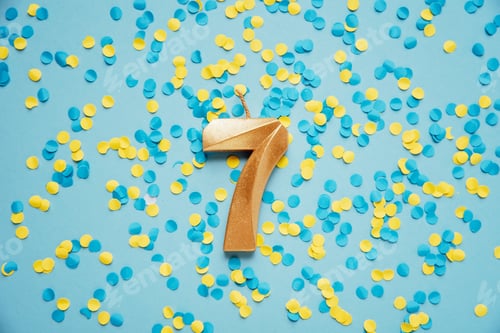 Preview: Number 7 seven golden celebration birthday candle on yellow and blue confetti Background.