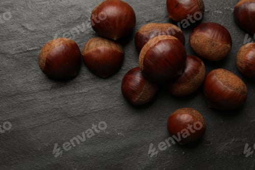 Preview: Roasted edible sweet chestnuts on grey textured table, flat lay. Space for text