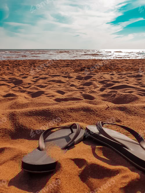 Preview: Idyllic beachscape featuring a pair of aqua blue sandals in the sand with a clear blue sky and ocean