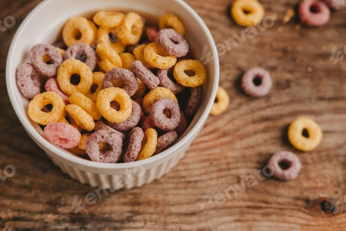 Preview: Colorful round fruit flakes in a white bowl scattered on a brown wooden table, top view