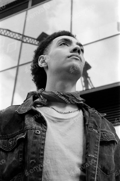 Preview: Young man wearing denim jacket and bandana looking up in black and white analog photo