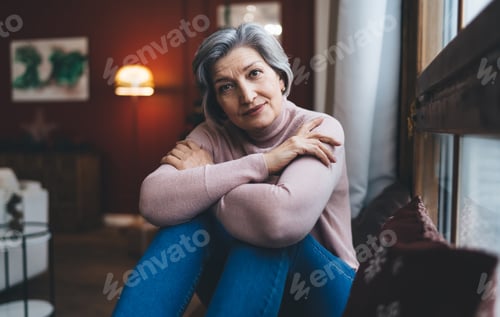 Preview: Smiling mature woman sitting on couch and in deep thoughts