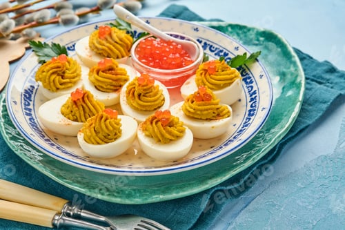 Preview: Stuffed eggs with red caviar and paprika on plate for appetizer easter table, top view, copy space.