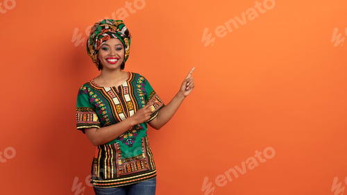 Preview: Pretty black woman in african costume pointing at free space