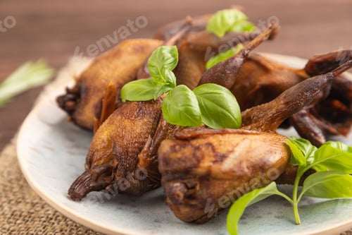 Preview: Smoked quails on a ceramic plate on a brown wooden background. Side view