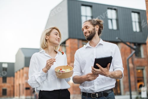 Preview: Charming woman holding a cardboard bowl with fresh organic salad and attractive man with tablet.