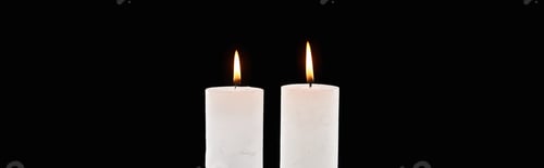 Preview: two burning white candles glowing isolated on black, panoramic shot
