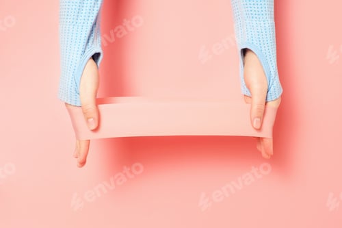 Preview: Hands stretching fitness elastic band on pink background close-up.