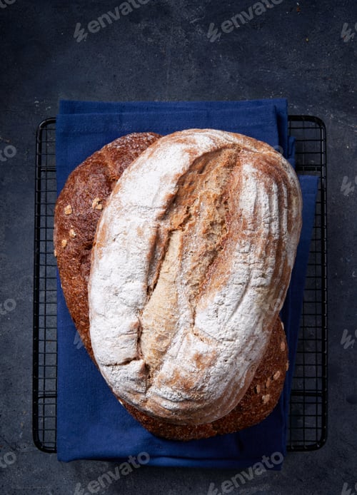 Preview: Two fresh homemade artisan breads stacked on dark gray surface.