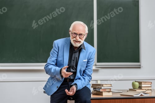 Preview: smiling grey hair professor sitting on table in lecture room