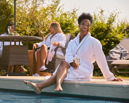 Preview: Mature Woman Wearing Robe Sitting With Feet In Pool Drinking Champagne On Spa Day