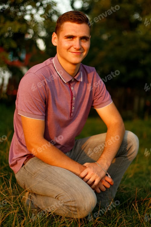 Preview: Happy young man. Portrait of smiling young brunette man in purple polo shirt seating outdoor on natu