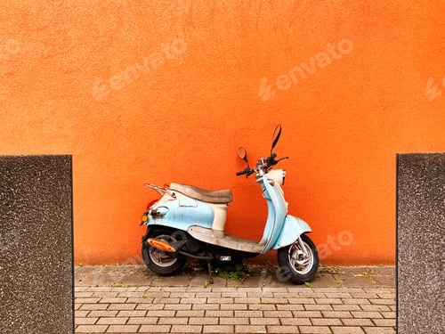 Preview: Blue motorcycle standing in front of orange textured monochrome wall in the city