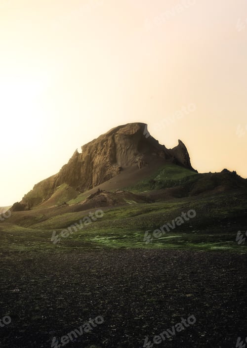 Preview: Mesmerizing vertical shot of a rocky mountain and green field under a clear sky at sunset