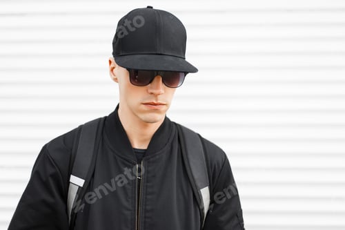 Preview: fashion man hipster in a black cap, stylish sunglasses, jacket with a black backpack. American guy.