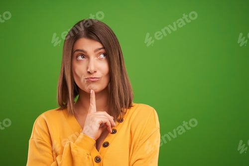 Preview: Close up of woman in yellow sweater thinking and pointing over green background