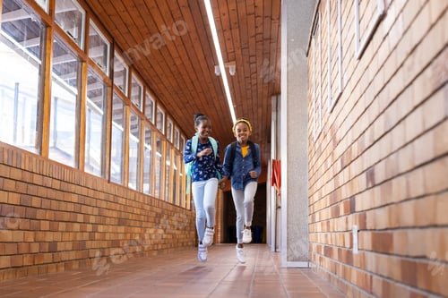 Preview: Running in school hallway, two african american girls with backpacks smiling and having fun