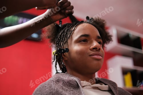 Preview: Afro young man semi-profile with half braided hair and hairstylist hands