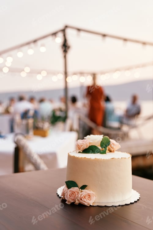 Preview: Wedding cake stands on a plate on the table against the backdrop of guests sitting at the table