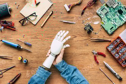 Preview: cropped image of man with amputee putting on robotic hand on table with tools