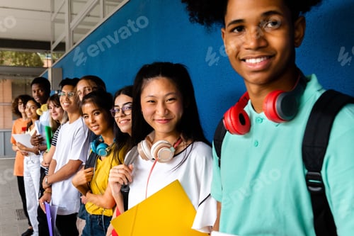 Preview: multiracial teen high school students looking at camera standing outside school building.