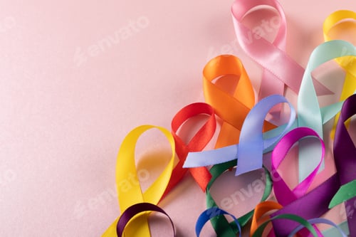 Preview: Close-up of various multicolored awareness ribbons against pink background, copy space