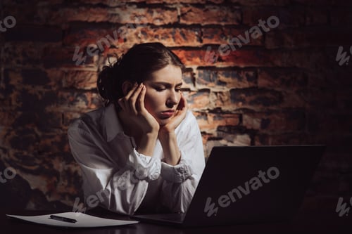Preview: Tired woman sitting at table with laptop and papers