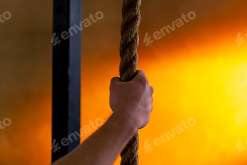 Preview: close-up in sports club of a hand holding ropes for exercise on a bright orange background