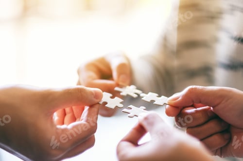 Preview: Closeup image of many people holding and putting a piece of white jigsaw puzzle together