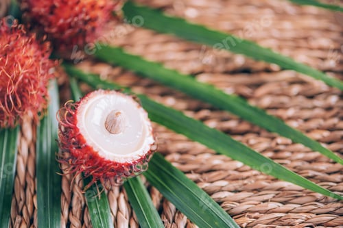 Preview: Rambutan fruits with palm leaves on rattan background. Top view. Copy space. Tropical fruit