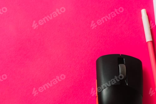 Preview: Close-up of a black wireless computer mouse and a pink pen on a vibrant hot pink background