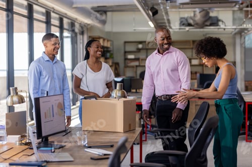 Preview: Team discussing project around office desk with charts and box, smiling together