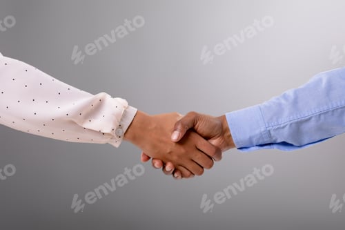Preview: Close up of businessman and businesswoman shaking hands against grey background