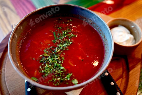 Preview: Russian traditional dish borscht with herbs and sour cream in a semicircular plate on a wooden board