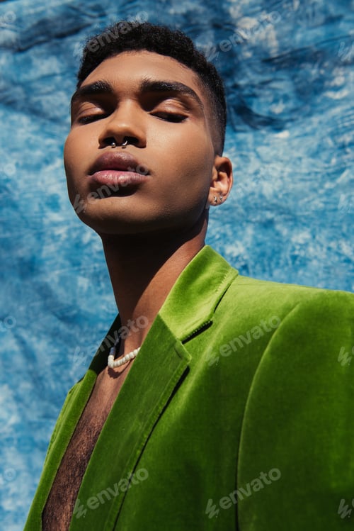 Preview: african american man with piercing posing in green blazer and beads near blue drape