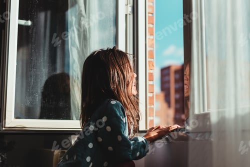Preview: Beautiful shot of a little girl with dark hair looking out the window on a sunny day
