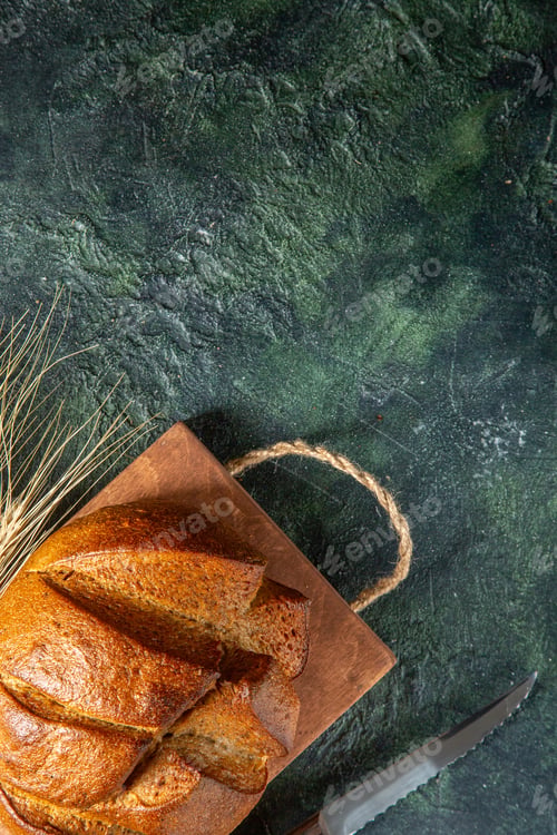 Preview: Top view of whole fresh black bread on brown wooden cutting board knife on dark colors background