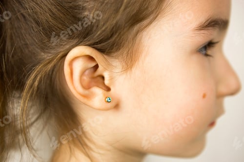 Preview: Ear piercing in a child - a girl shows an earring in her ear made of a medical alloy