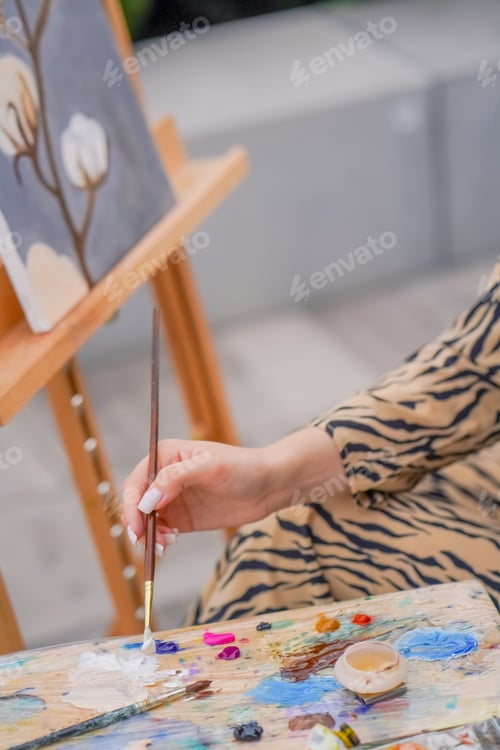 Vista previa: Close-up of a girl artist brushes oil paint on a painting standing on an easel in studio