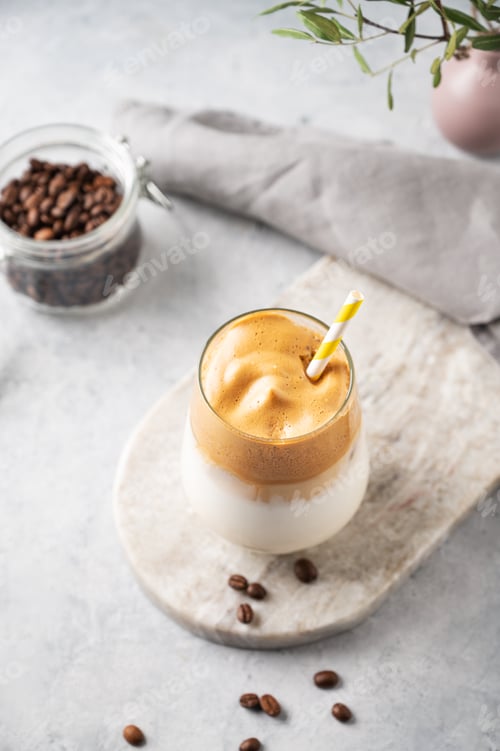 Preview: Dalgona coffee with foam in a glass with coffee beans on light marble background with branches