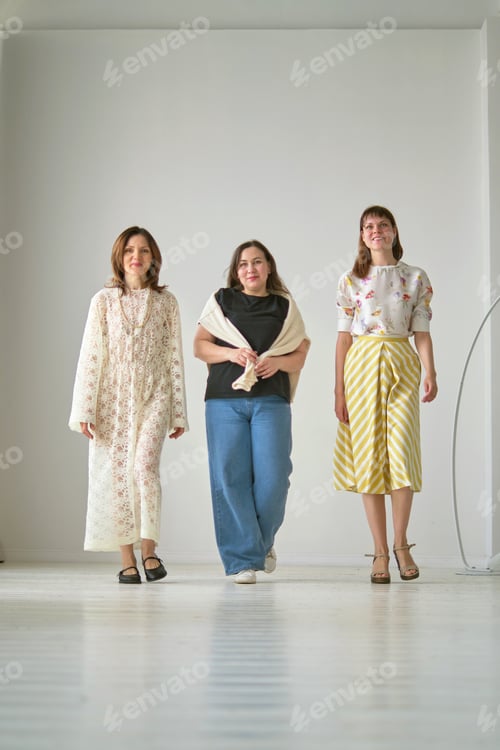 Preview: Three women walk forward in a minimalist room, each showcasing a unique fashion style. Their