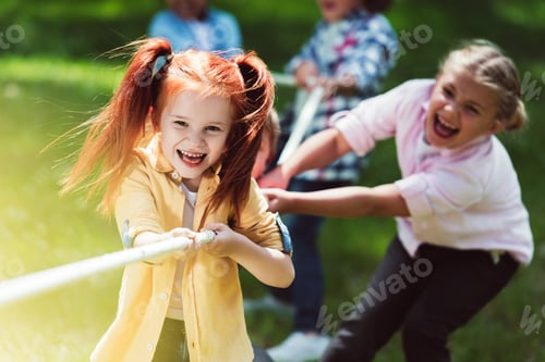 Preview: adorable cheerful girls playing tug of war in park