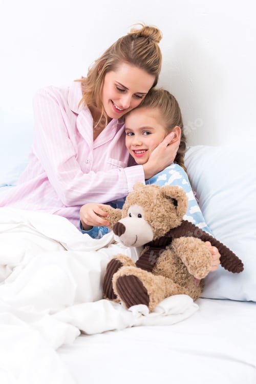 Preview: mother hugging daughter with teddy bear on bed at home