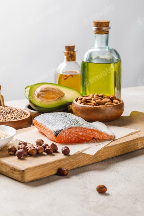 Preview: raw salmon, nuts and avocado on wooden chopping board near oil isolated on grey, ketogenic diet menu