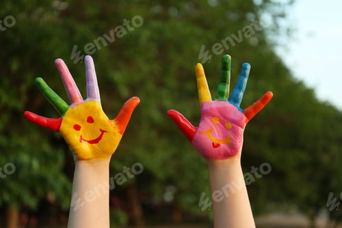 Preview: Kid with smiling face drawn on palms in green park, closeup