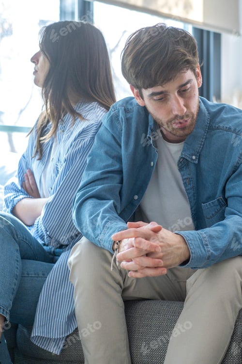 Preview: Unhappy couple sitting on sofa at home looking to opposite directions sad.