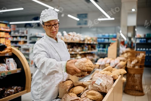 Preview: Supermarket baker arranging fresh bread on a shelf.