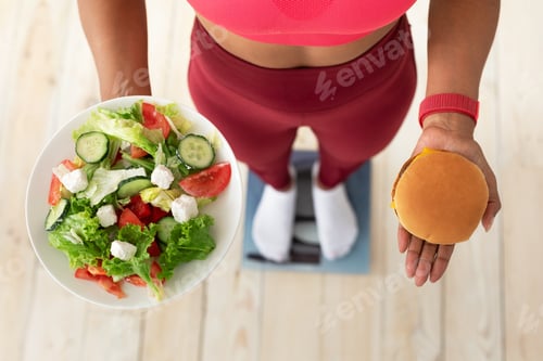 Preview: Girl Choosing Between Salad And Burger Standing On Scales Indoors